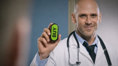 A smiling bald doctor wearing a white coat and stethoscope holds up a capsule-shaped Buy Button like a prescription.